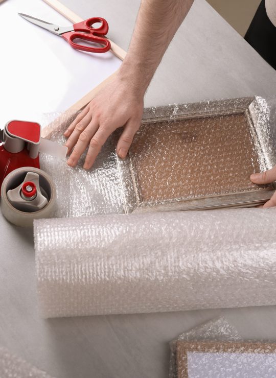 Man,Covering,Photo,Frame,With,Bubble,Wrap,At,Light,Grey