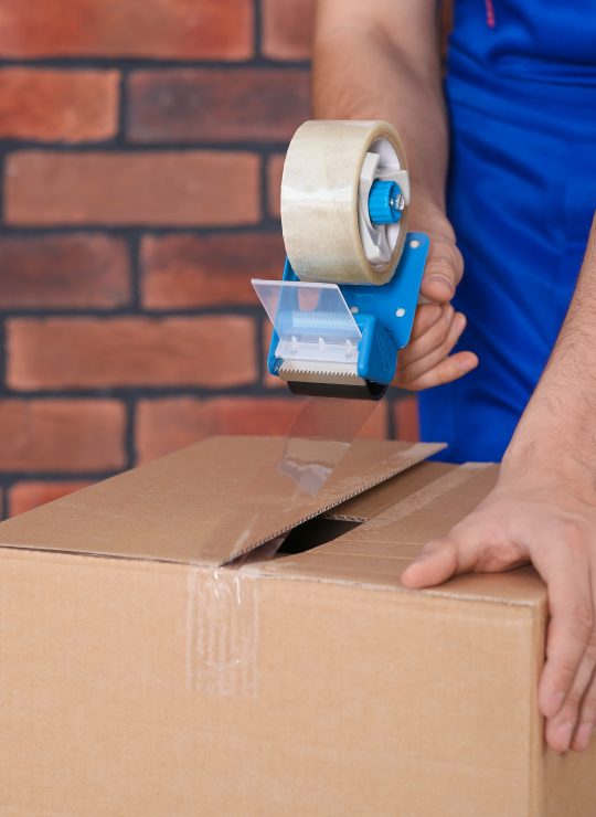 Worker,Taping,Box,With,Adhesive,Tape,Dispenser,Near,Brick,Wall,